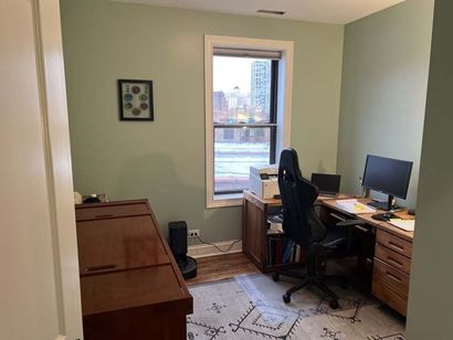 Small home office with a desk, chair, window, and rug; walls are pale green.
