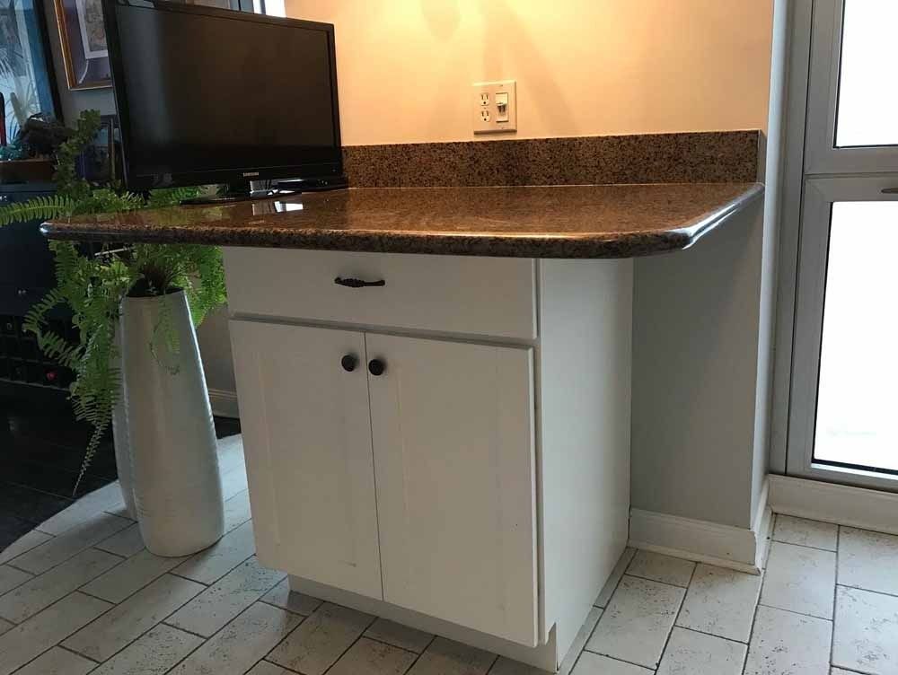 White cabinet with brown countertop, holding a TV, near a window.