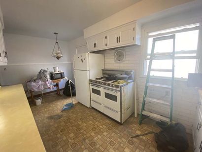 Kitchen with white appliances, cabinets, and a stove. A ladder leans against a window.