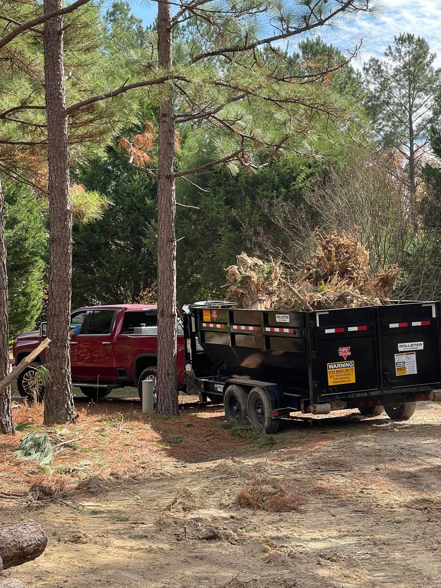 Red pickup truck and black utility trailer parked among pine trees in a wooded area