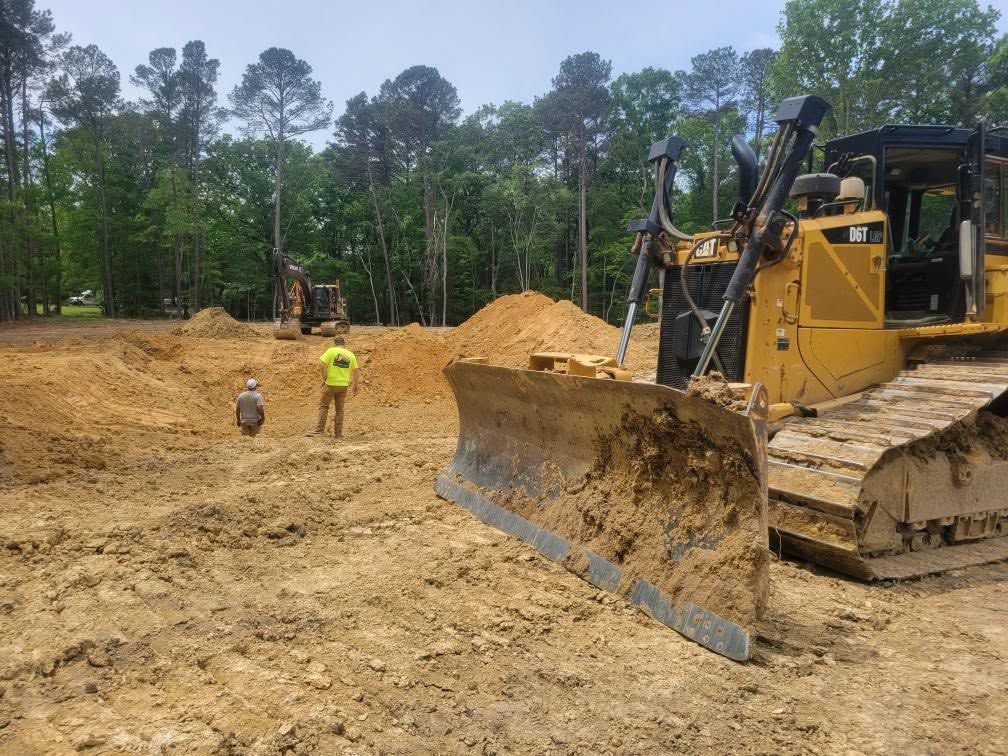 Bulldozer on a dirt construction site with workers and large sand piles under cloudy sky