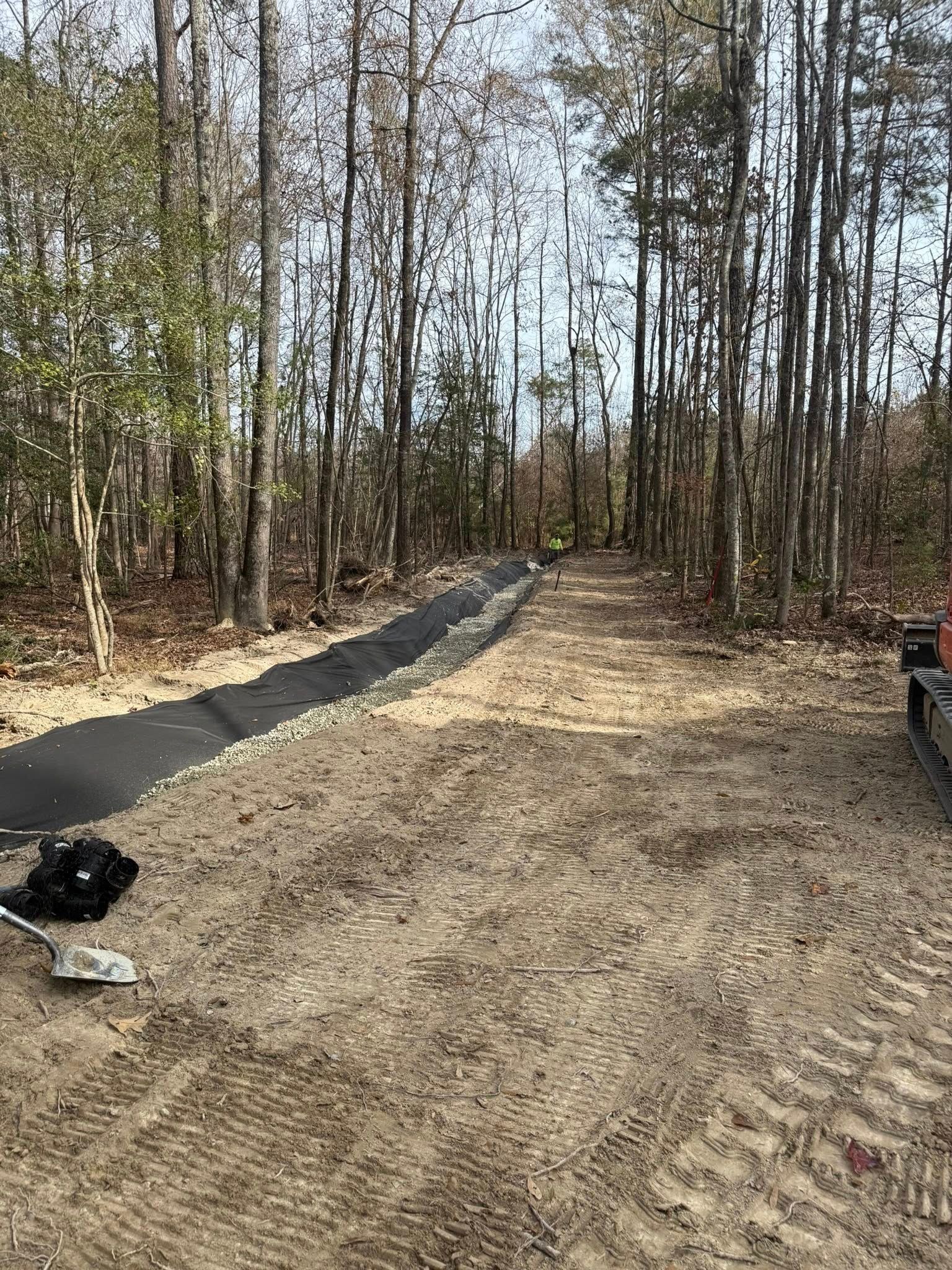 Wooded dirt lot with a gravel path, black bag on the left, and a vehicle edge on the right