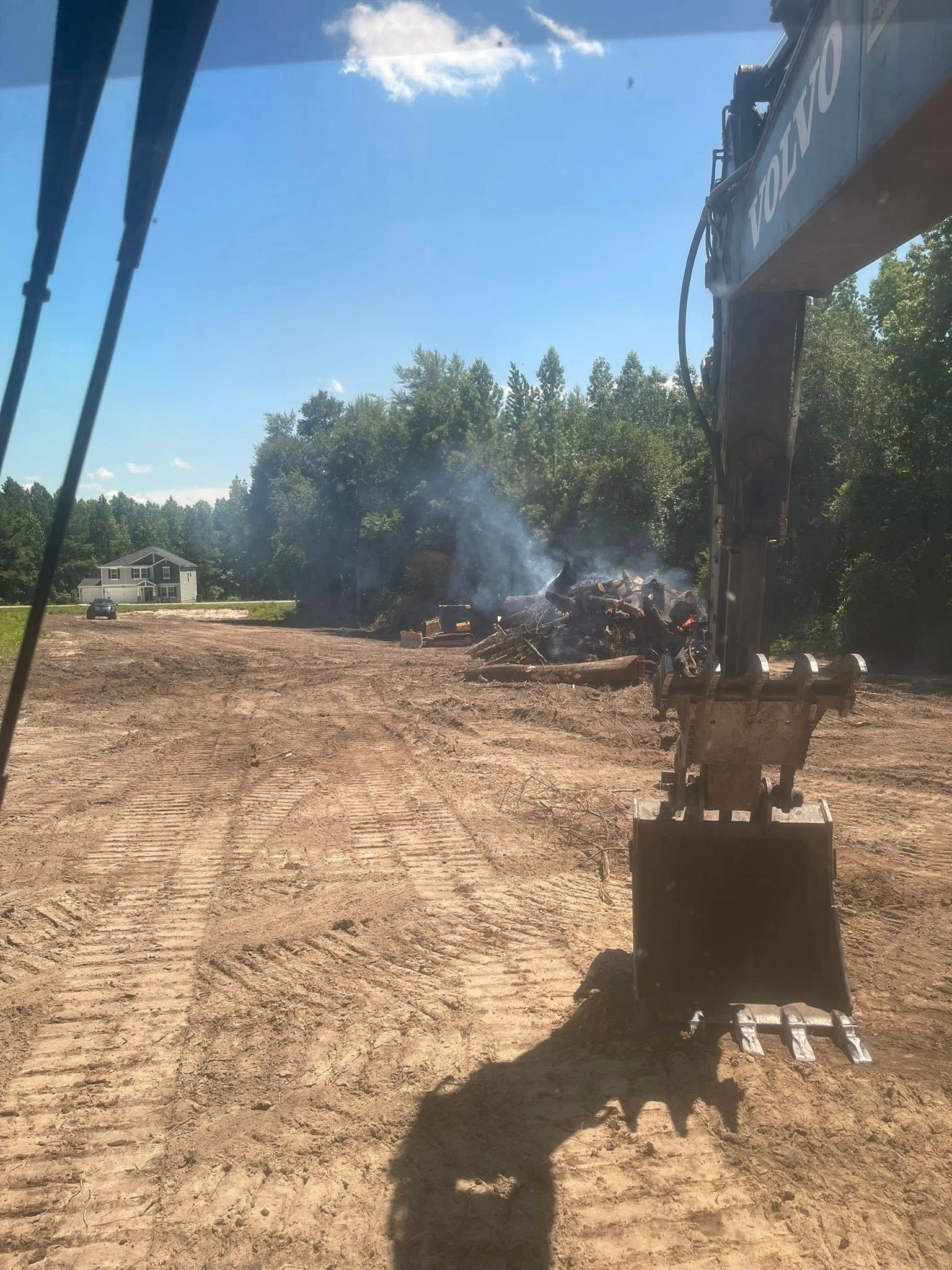 Construction excavator working on a dirt lot with smoke rising in the background under a blue sky