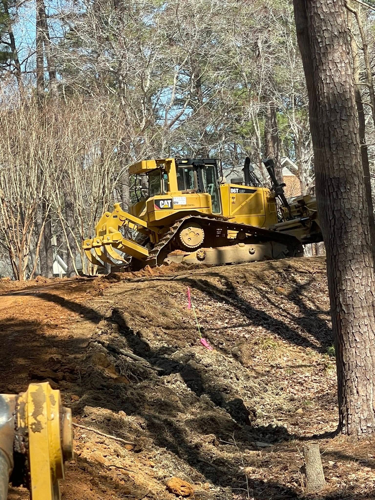 Yellow bulldozer on a wooded dirt slope, clearing earth near trees