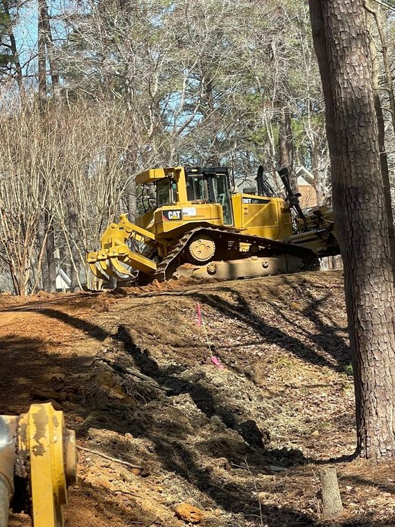 Yellow bulldozer clearing dirt on a wooded hillside with bare trees in the background