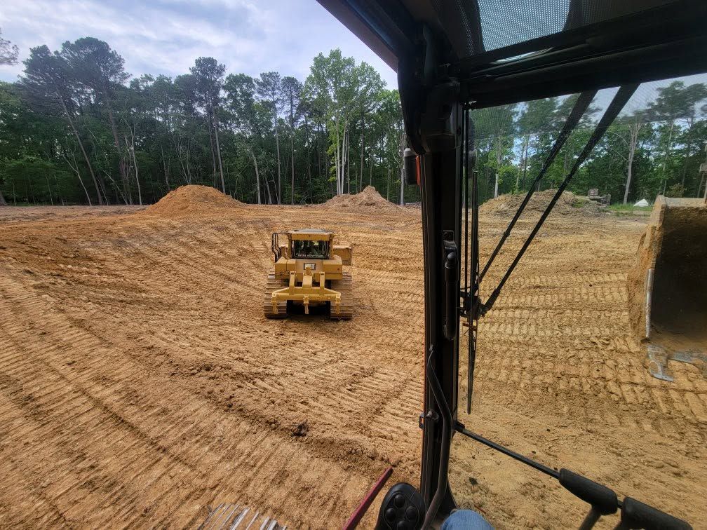 Bulldozer grading a sandy construction site with tree line in the background