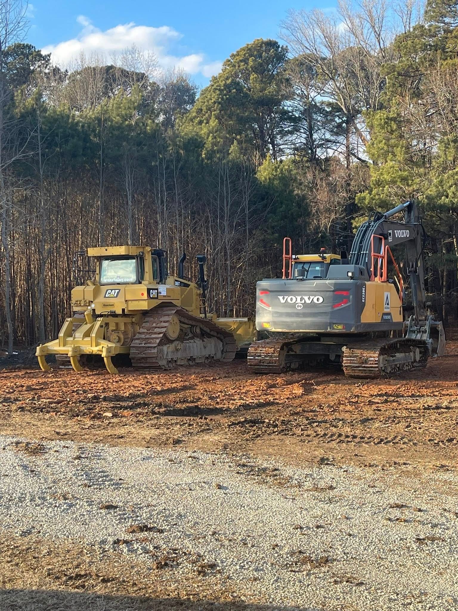 Yellow bulldozer and gray excavator on muddy ground in a wooded construction site