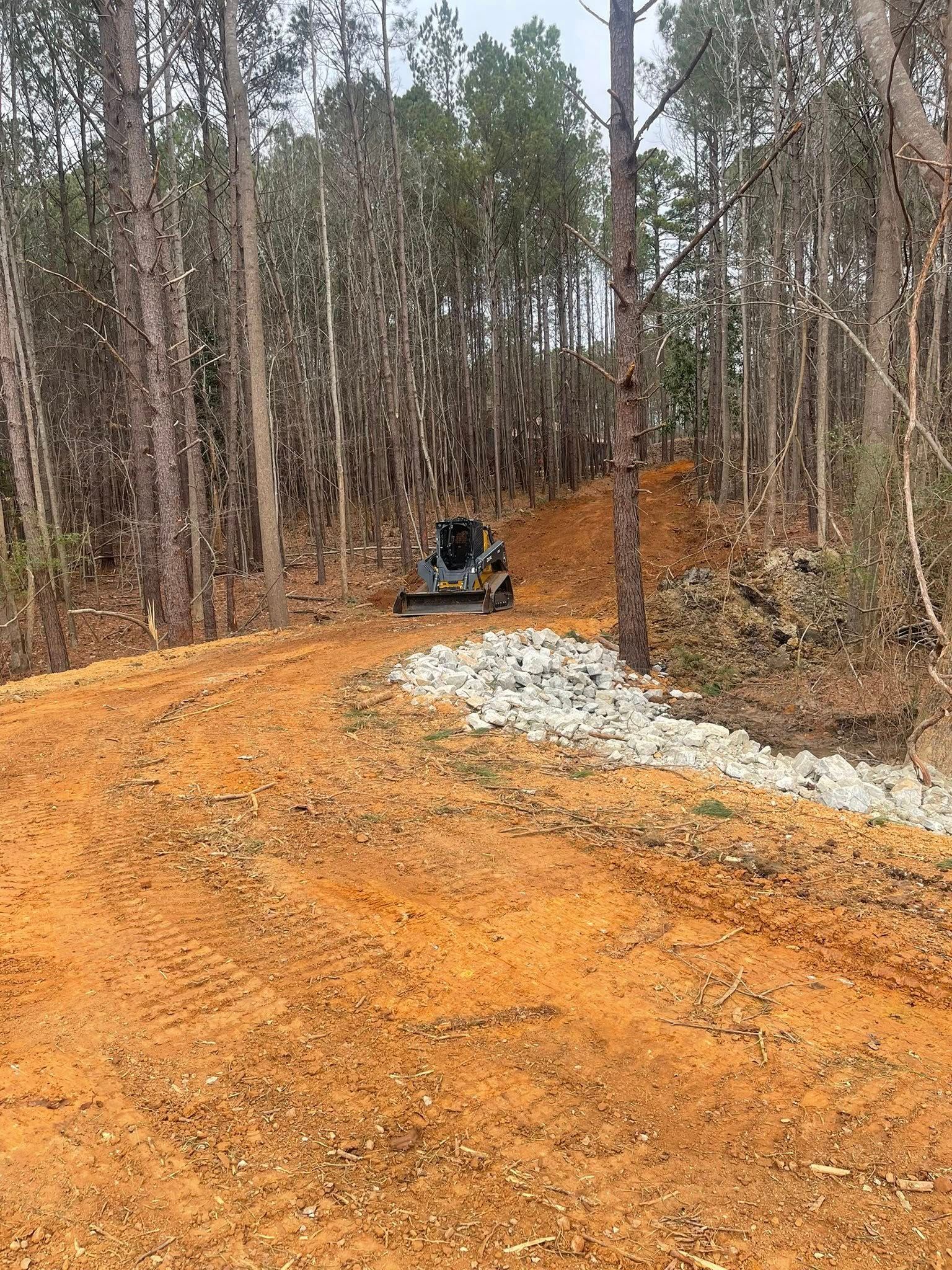 Dirt road in a pine forest with a small bulldozer and a gravel pile on the right side