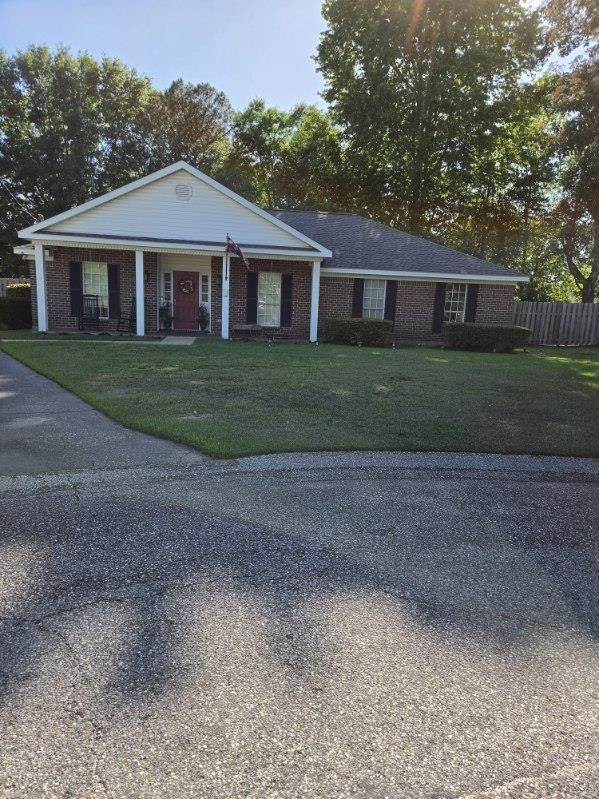 Single-story brick house with white porch columns, front lawn, and driveway in bright sunlight