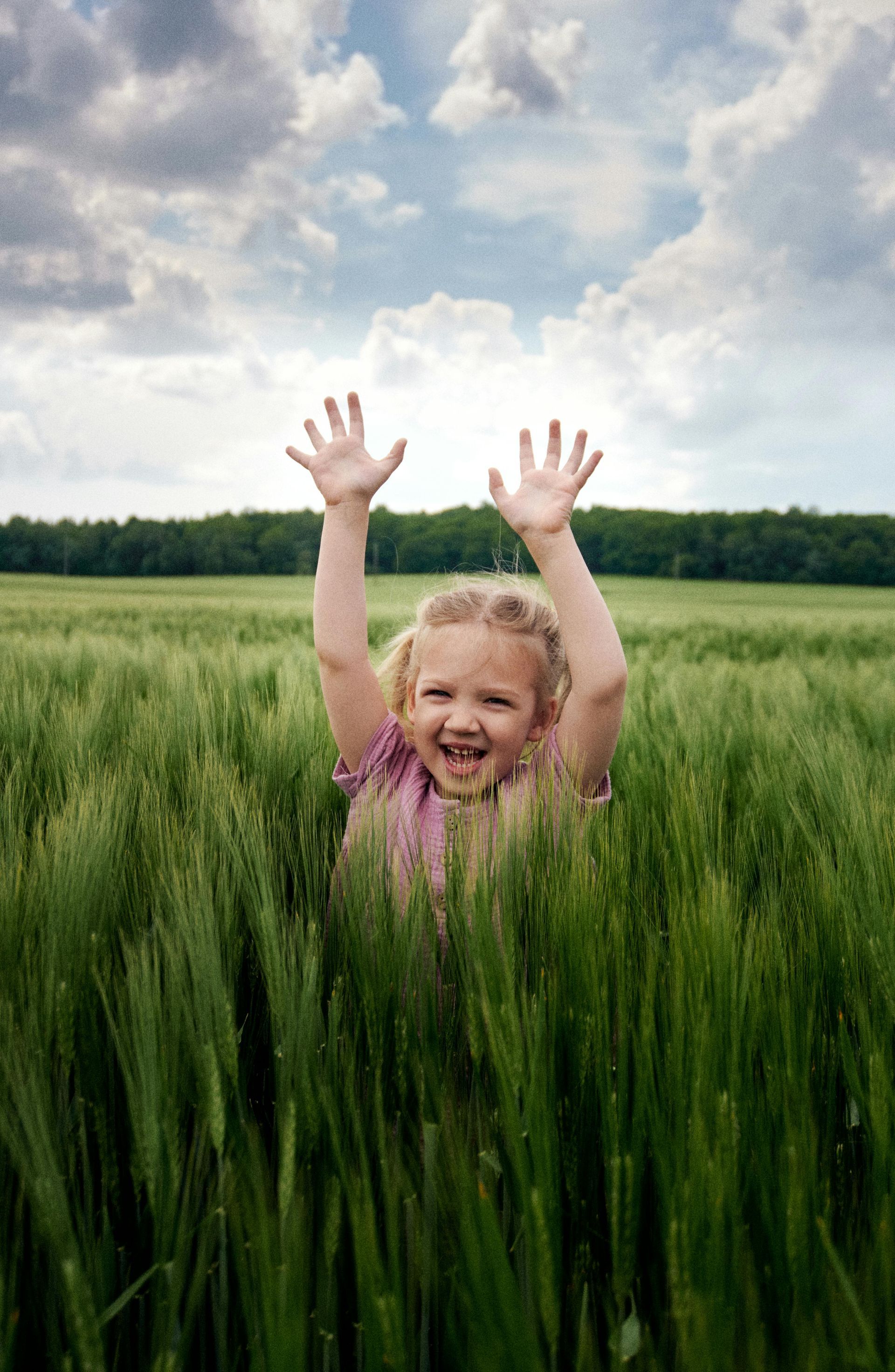 A little girl is standing in a field with her hands in the air.