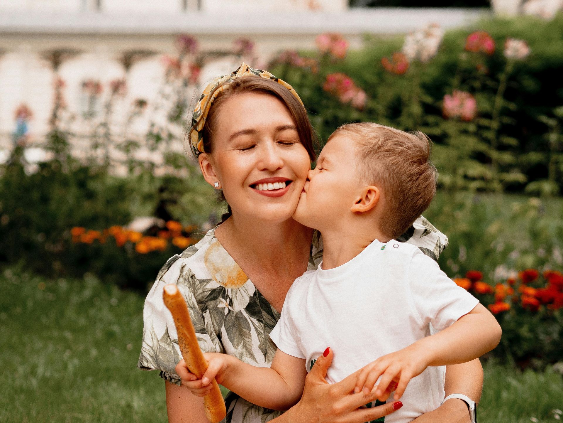 A little boy is kissing a woman on the cheek while holding a loaf of bread.