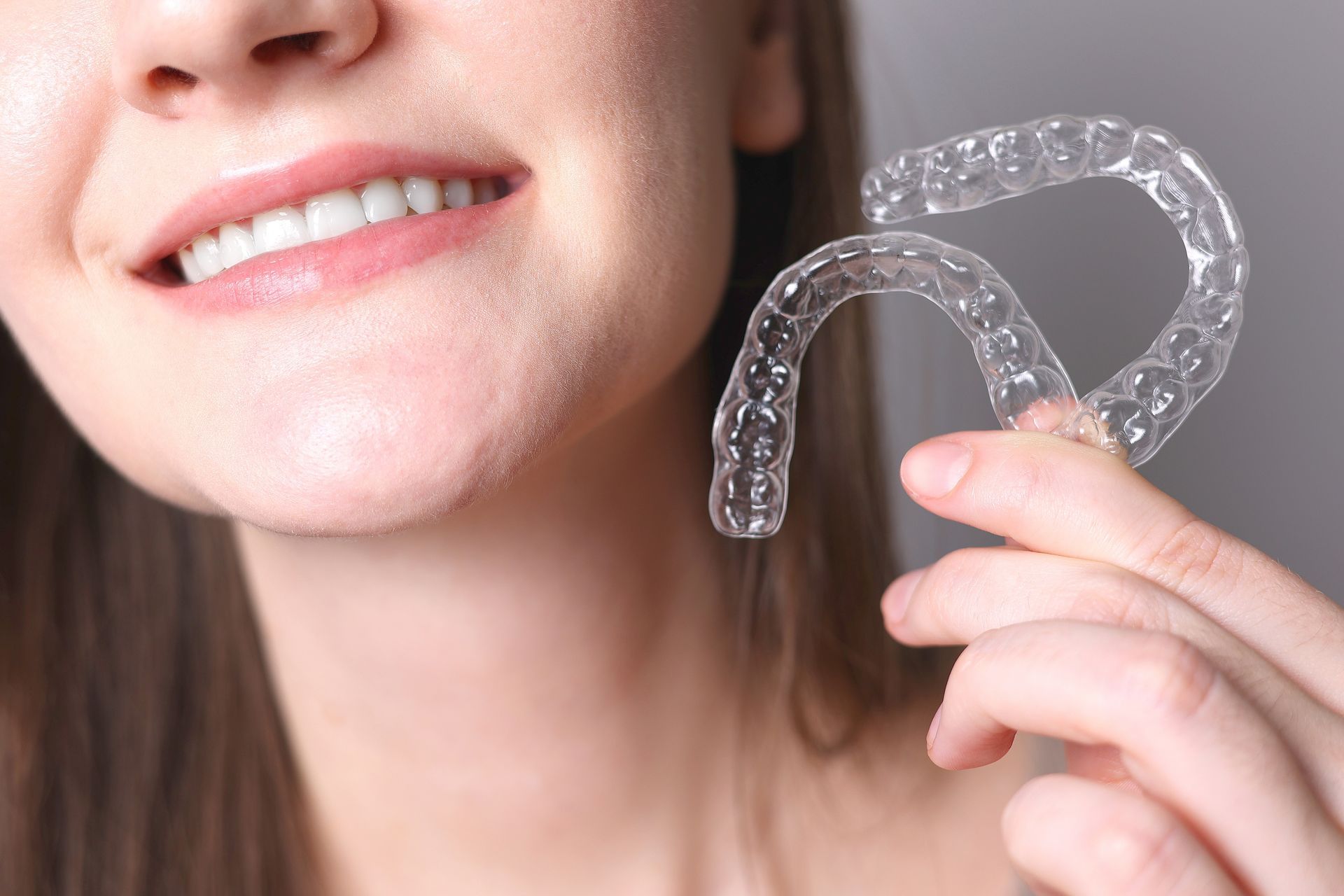 A woman is smiling while holding a clear retainer in her hand.