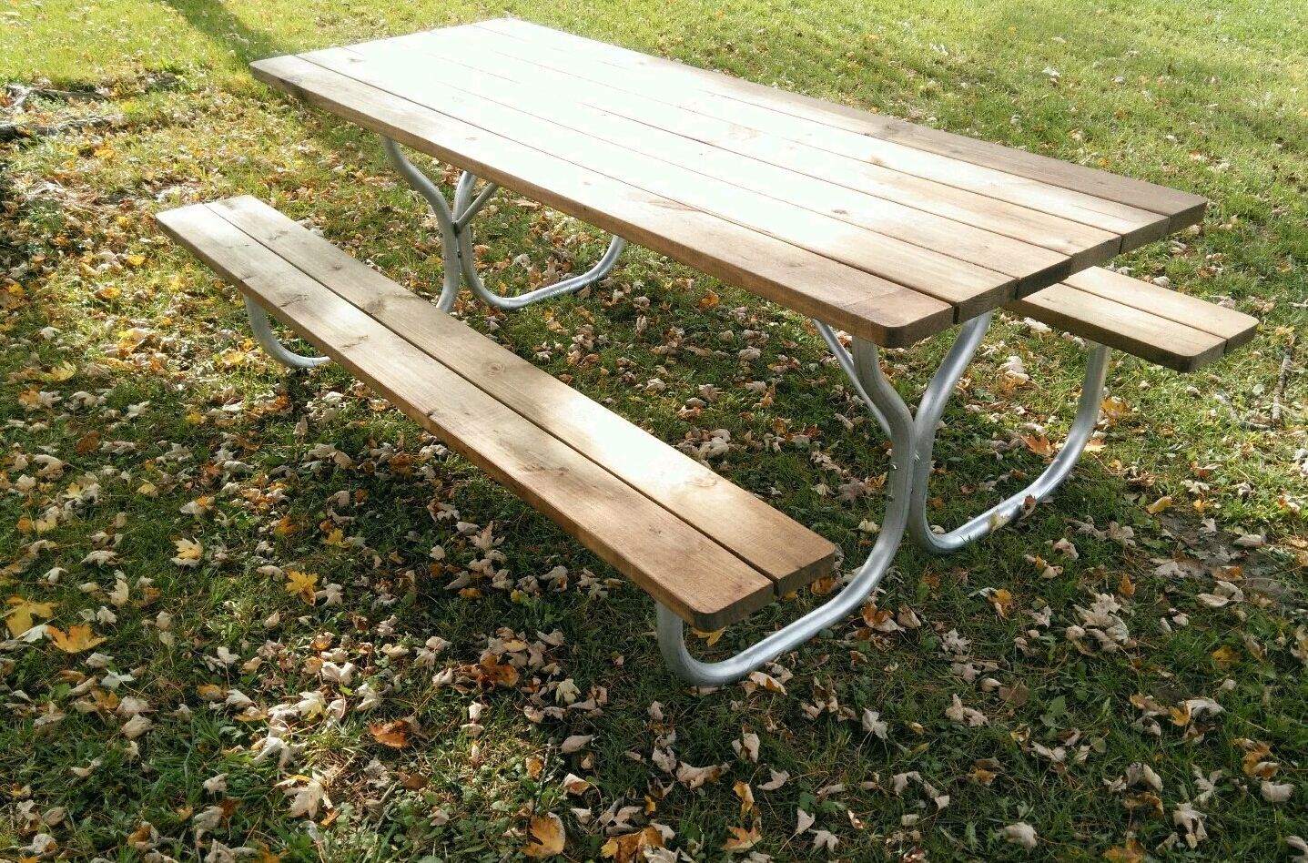 Picnic table with wooden top and benches, metal frame, on grass.
