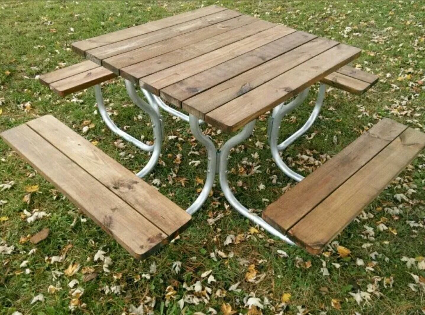Square picnic table with wooden top and benches, set on a grassy lawn.