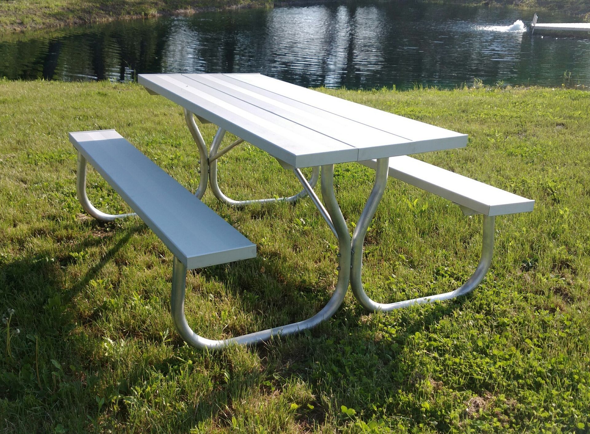 Picnic table with silver frame and top in grassy area by a pond.