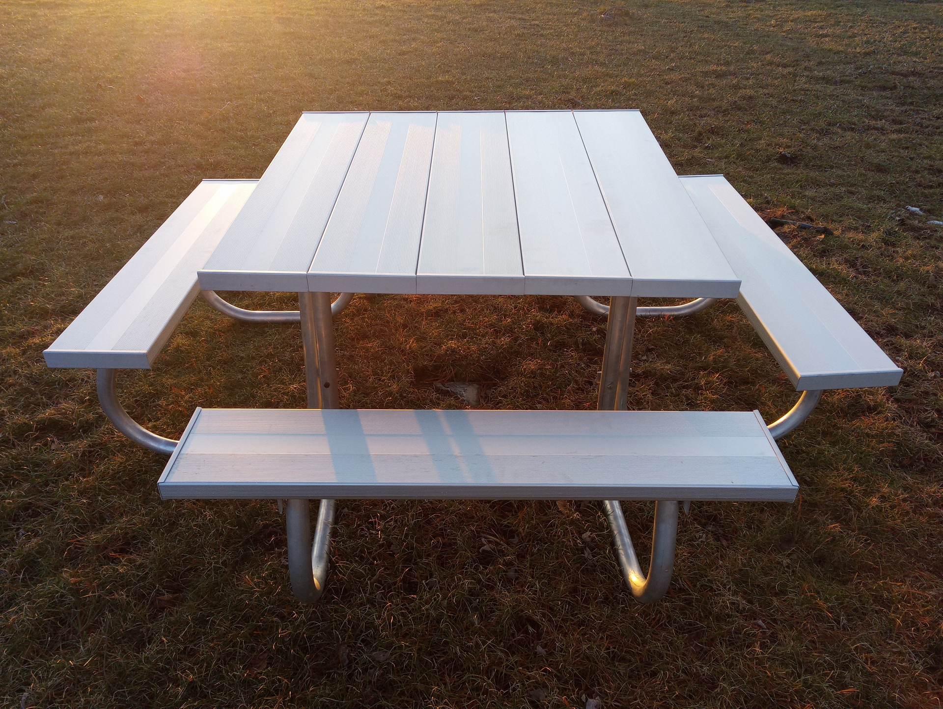 White aluminum picnic table with attached benches on a grassy field.