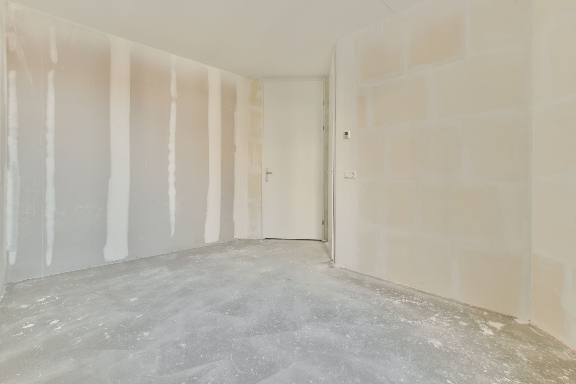 Empty room under construction with unfinished drywall, white walls, and a bare concrete floor
