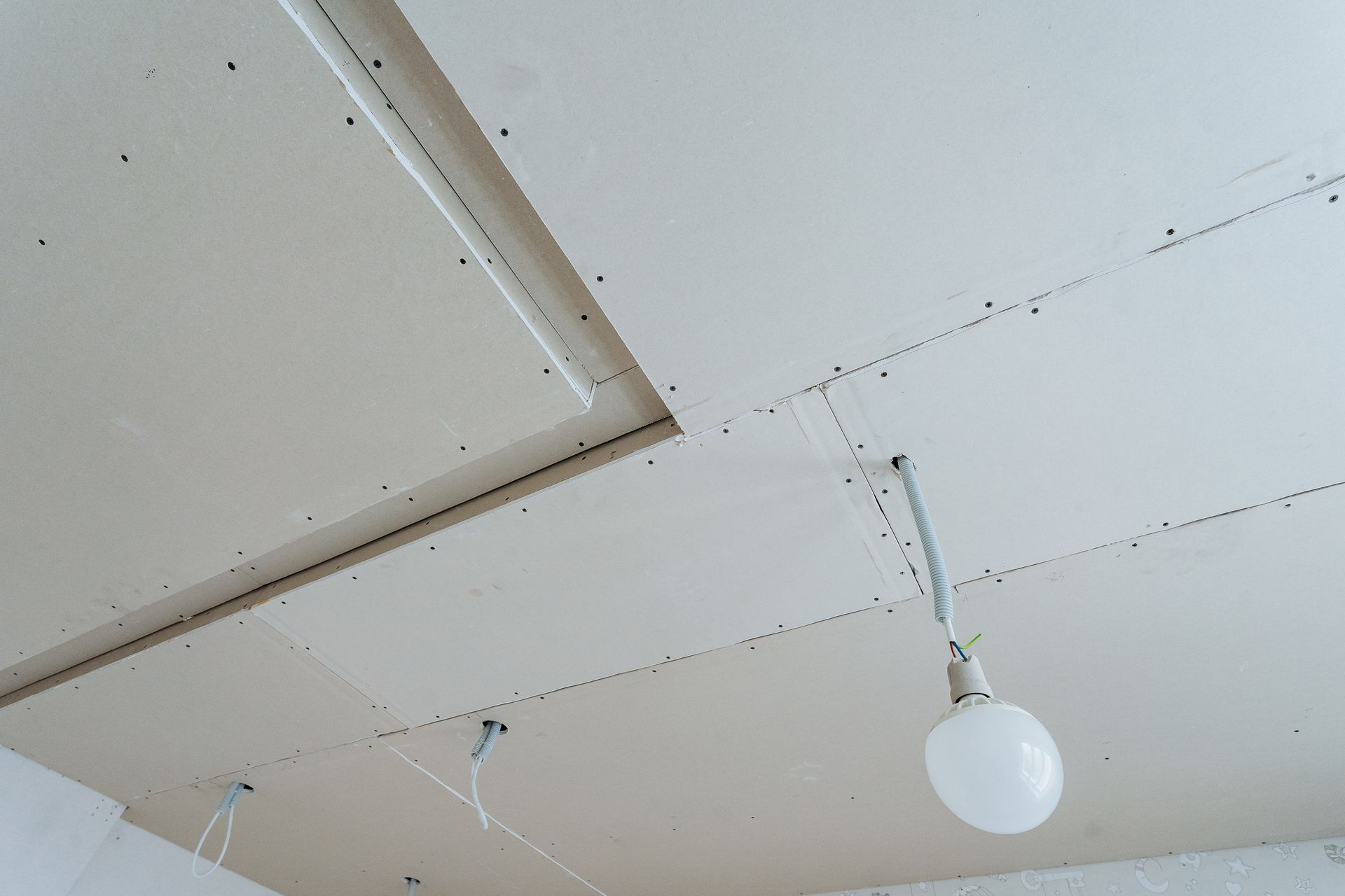 Ceiling with white panels, exposed wiring, and a hanging round light bulb