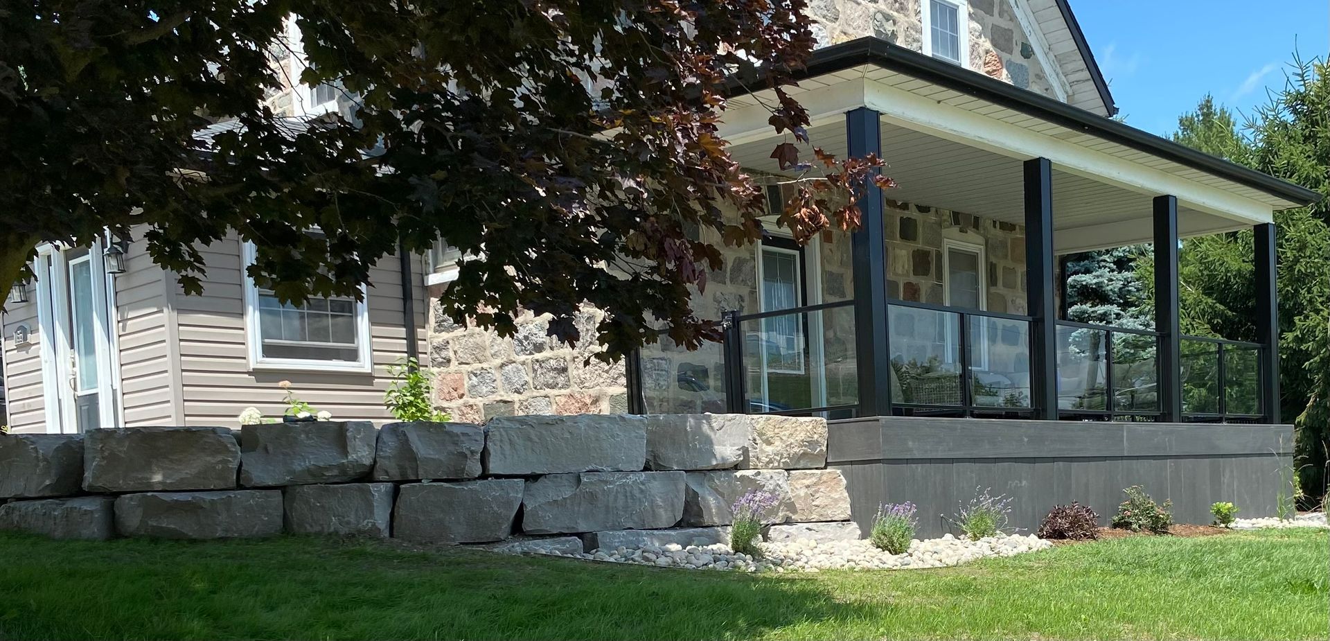 Stone house with porch, glass railing, and stone wall in front.
