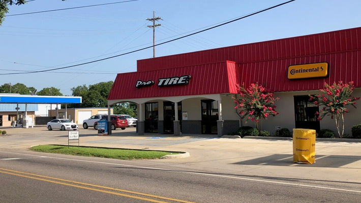A tire shop with a red roof and sign, a gas station, and cars parked in front.