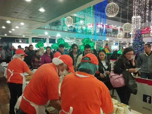 Mostrador abarrotado de un aeropuerto, donde el personal con uniformes naranjas atiende a los viajeros bajo luces festivas