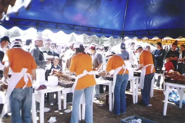 Voluntarios con camisetas naranjas sirviendo comida en un evento al aire libre bajo una carpa