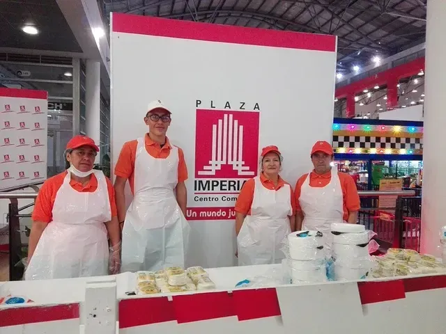 Cuatro vendedores con gorras y delantales rojos detrás de un puesto blanco y rojo con el letrero Plaza Imperial.