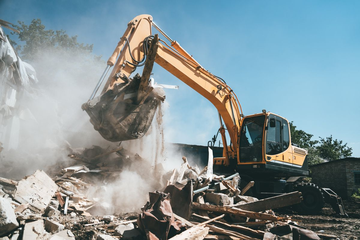 Excavator demolishing a rubble pile, with dust rising at a construction site.