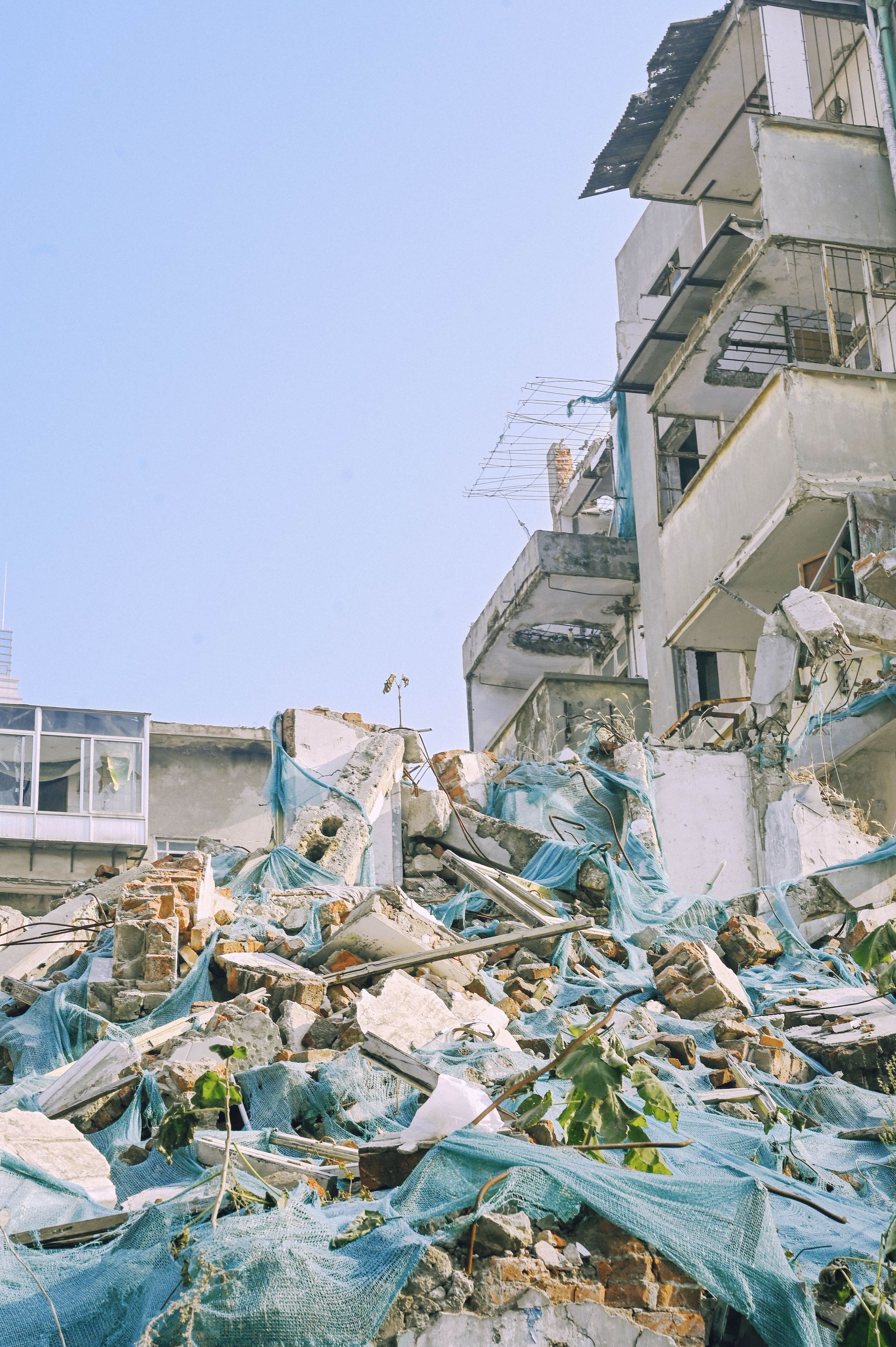 Collapsed building rubble beside damaged apartment balconies under a clear blue sky