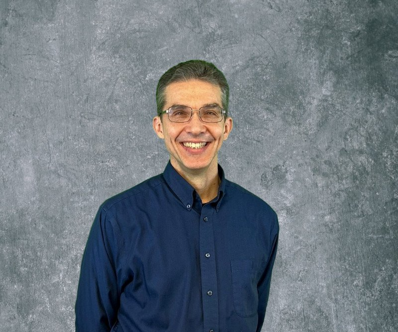 Smiling man in a navy shirt standing against a gray textured backdrop