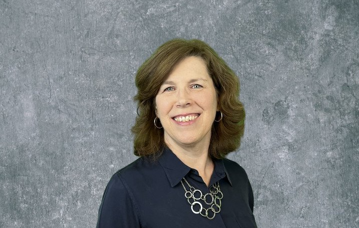 Smiling woman in a dark blouse and silver necklace against a gray studio backdrop