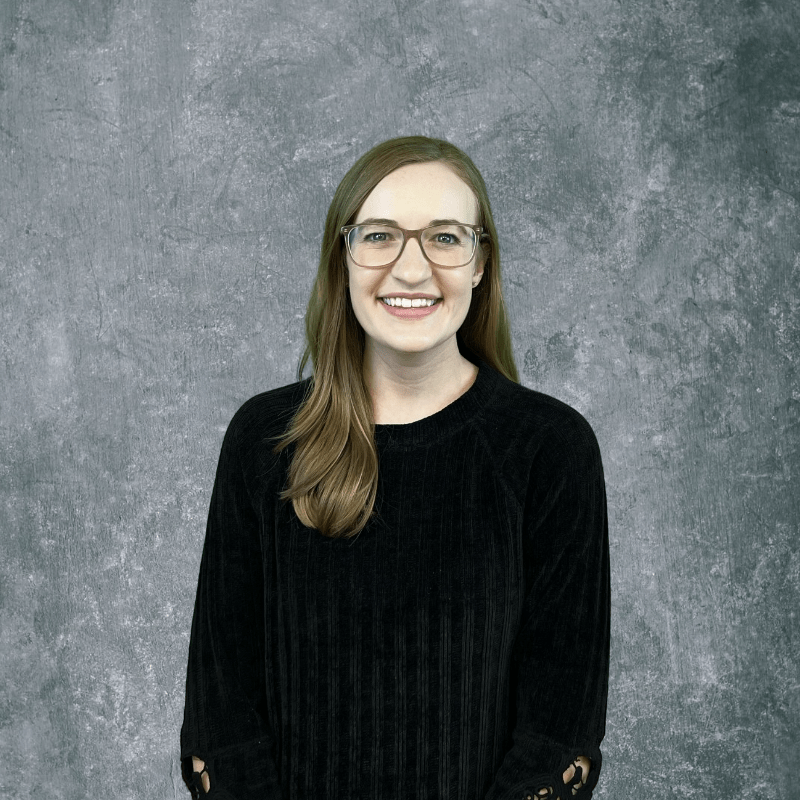 Portrait of a smiling person in glasses and a black sweater against a gray backdrop