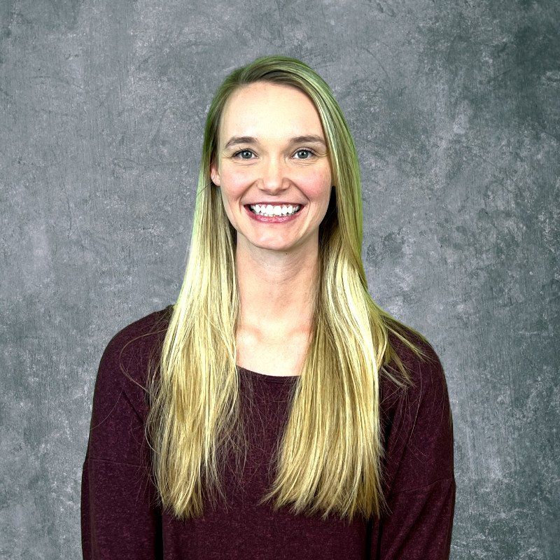 Smiling woman with long blonde hair in a maroon top against a gray backdrop