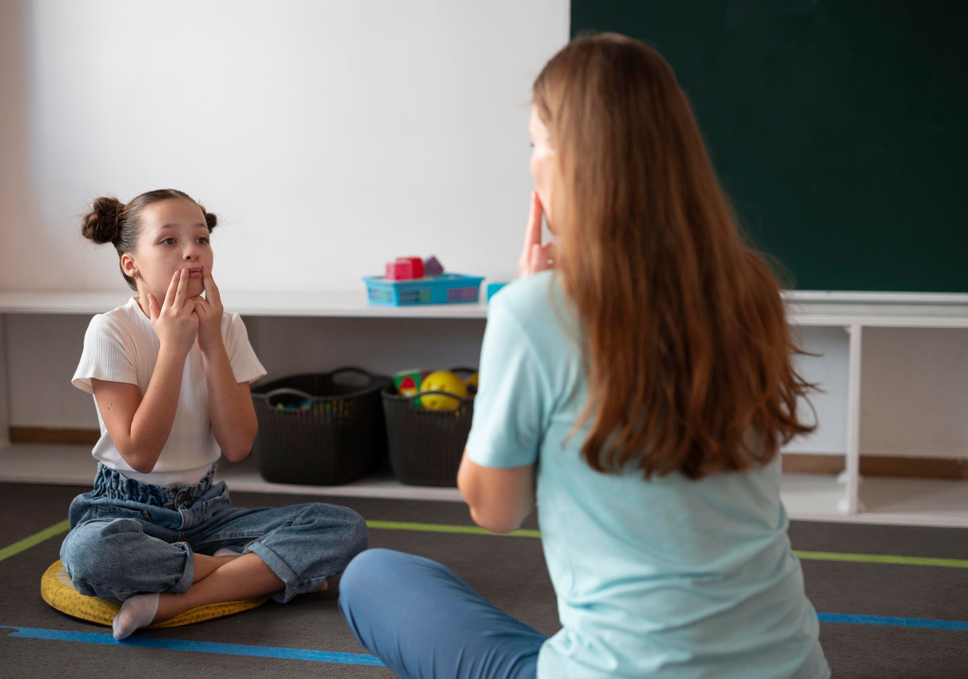 Two people seated on a classroom rug, facing each other during a conversation or lesson.