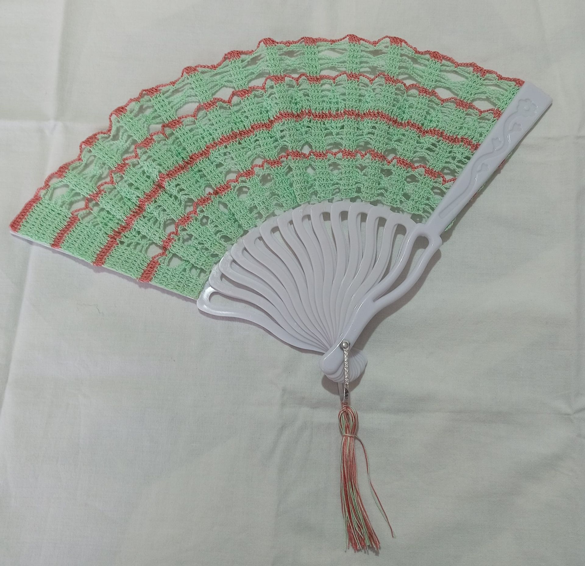 Ventaglio pieghevole decorativo con pizzo verde e rosso su sfondo di stoffa chiara.