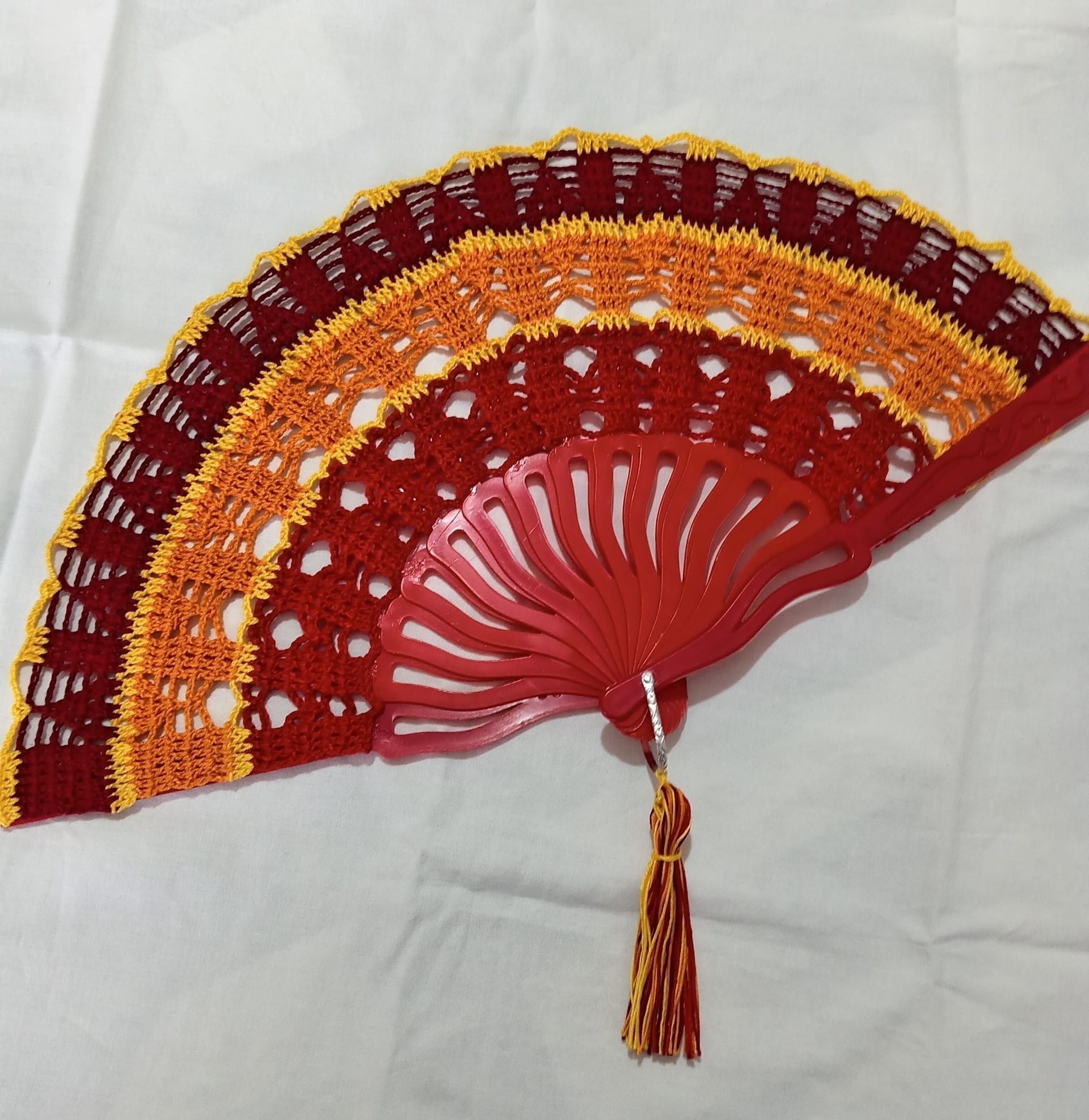 Ventaglio decorativo rosso e arancione con nappa su sfondo di stoffa bianca