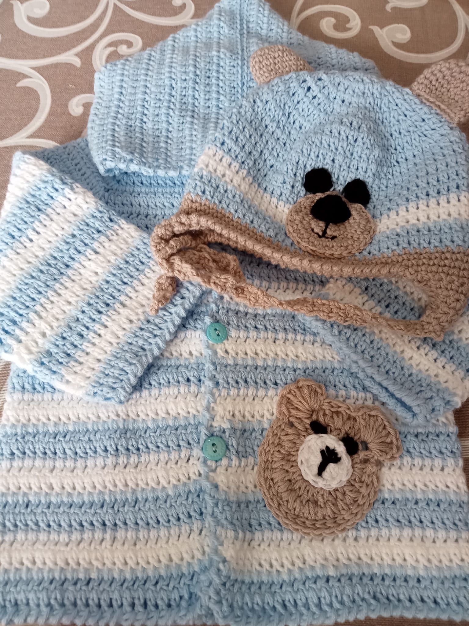 Maglioncino e cappellino per neonato a righe blu e bianche con decorazioni a forma di orsetto su sfondo fantasia.