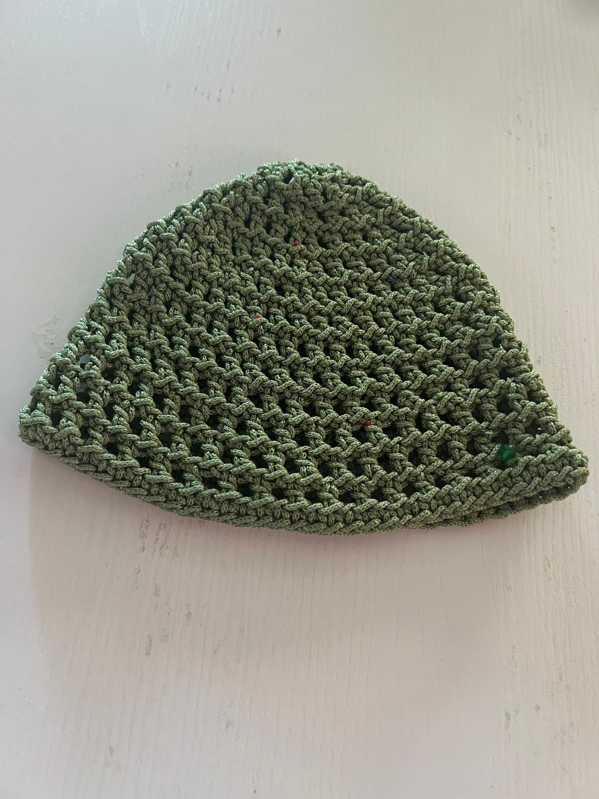 Berretto verde lavorato all'uncinetto a forma di cupola su uno sfondo chiaro e uniforme.