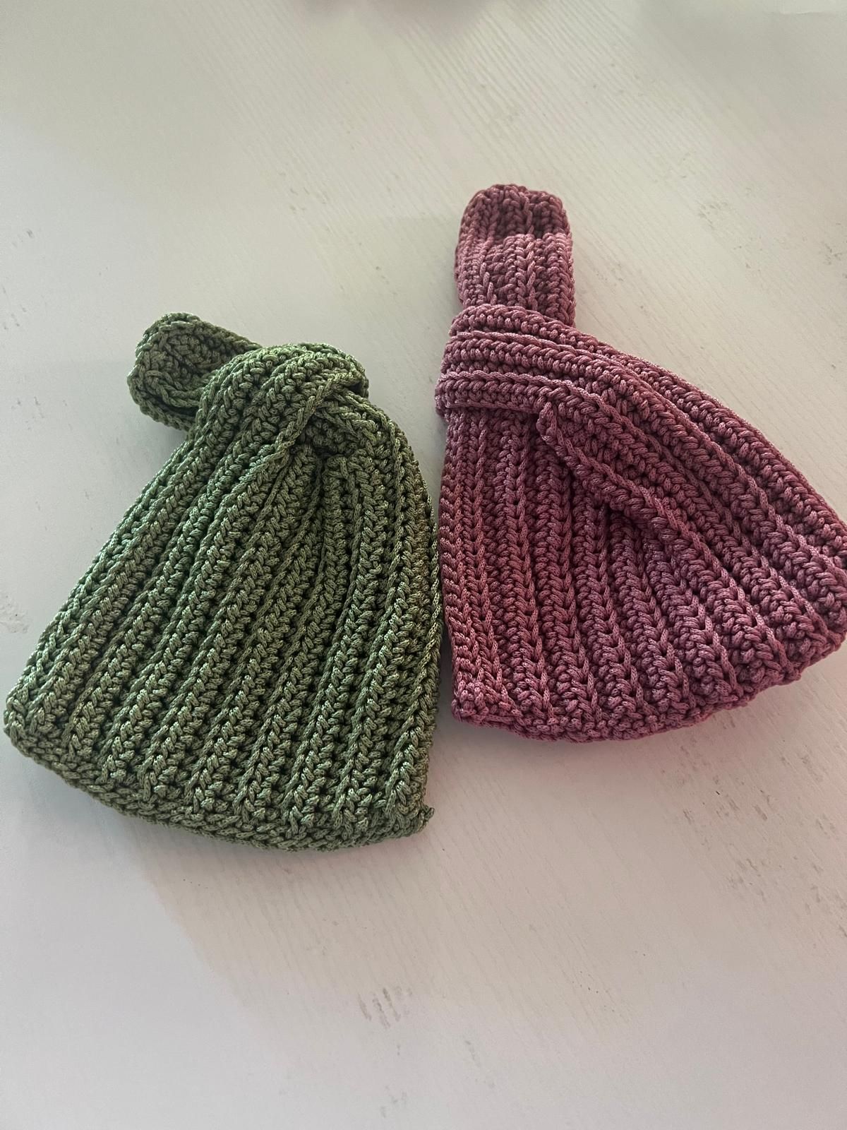 Due sacchetti a forma di nodo lavorati a maglia, uno verde e uno rosa, su una superficie bianca