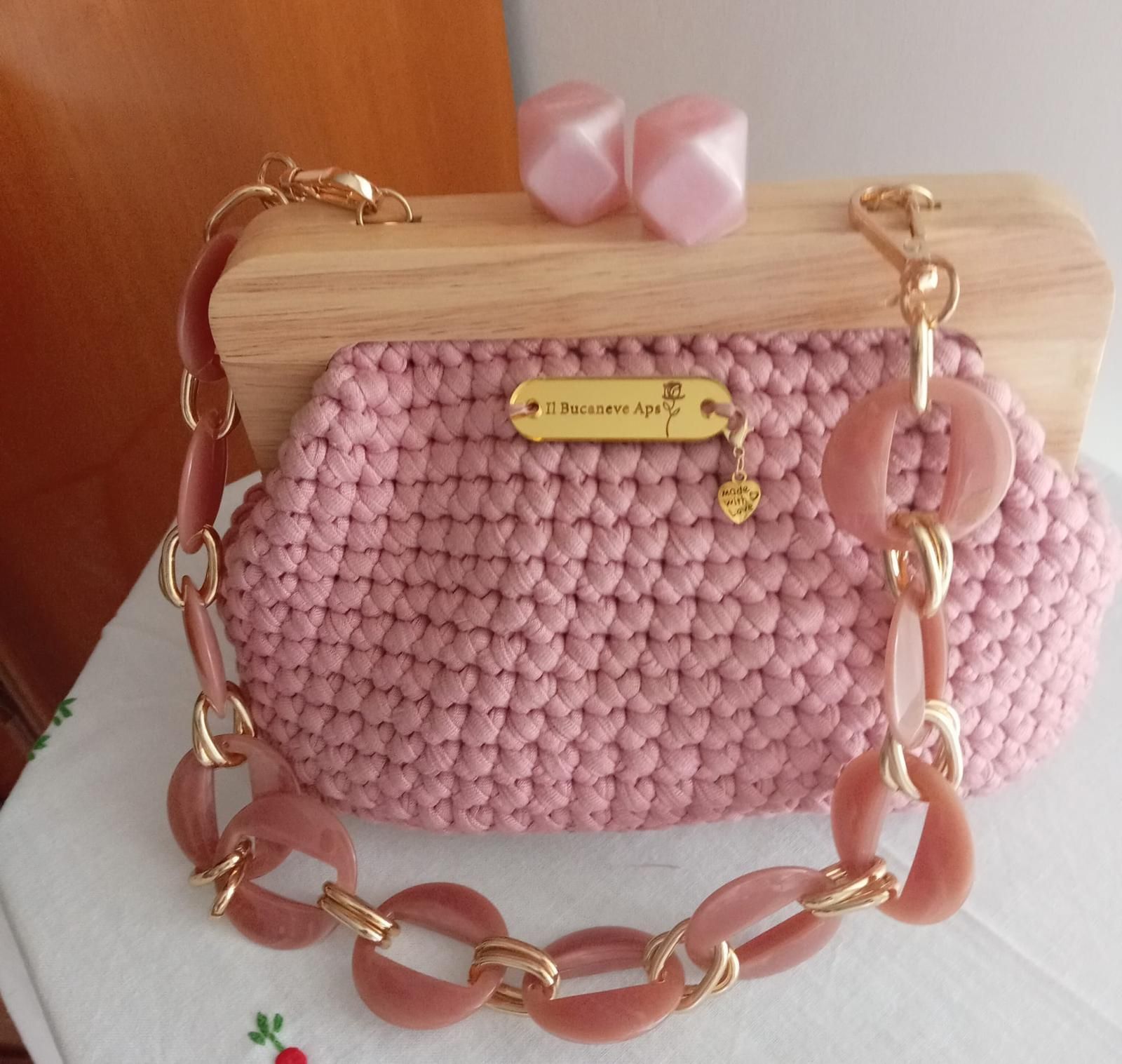 Borsa rosa all'uncinetto con manico in legno e tracolla a catena spessa su sfondo bianco.