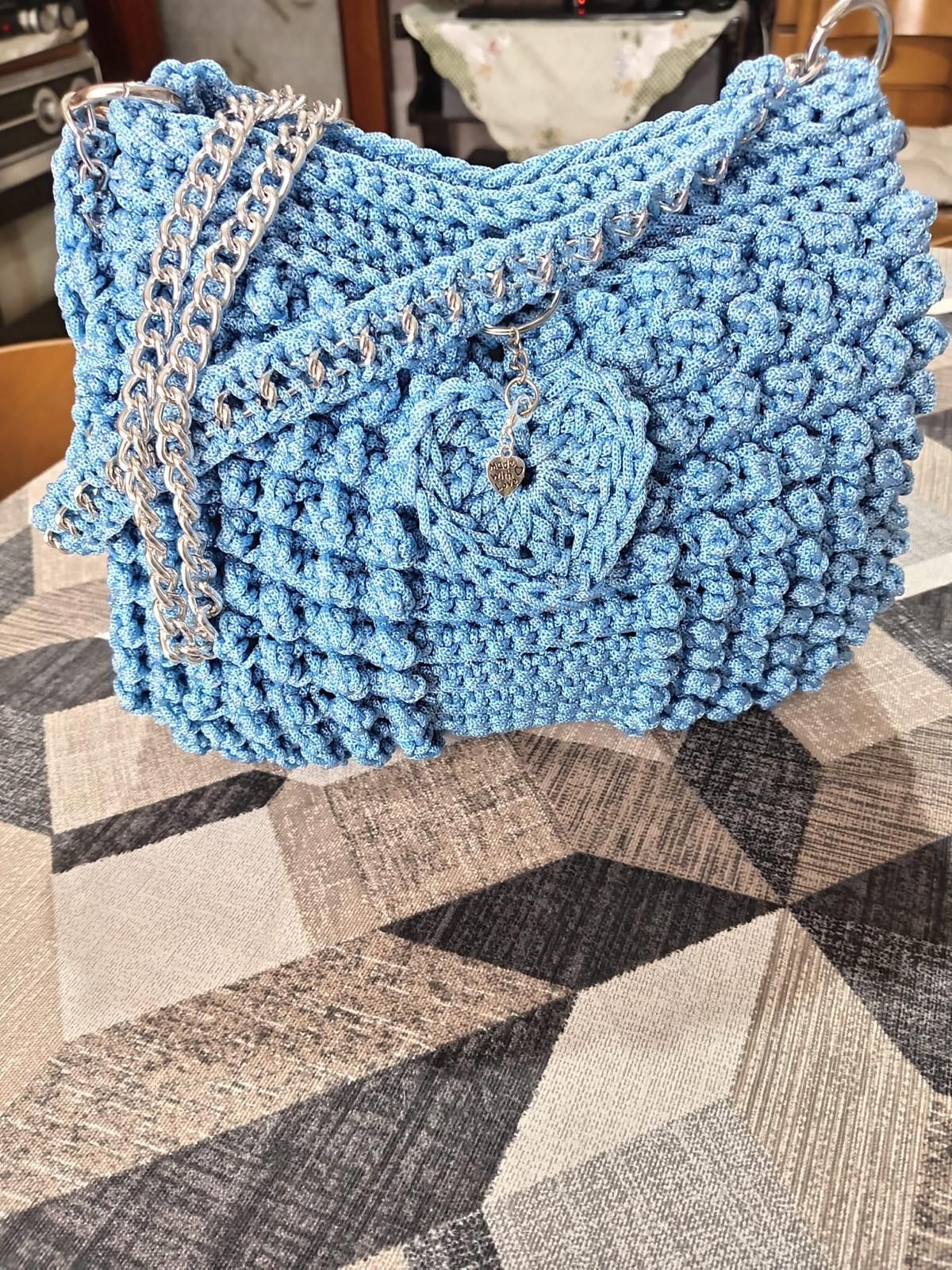 Borsa blu all'uncinetto con patta e tracolla intrecciata su una tovaglia a quadri.