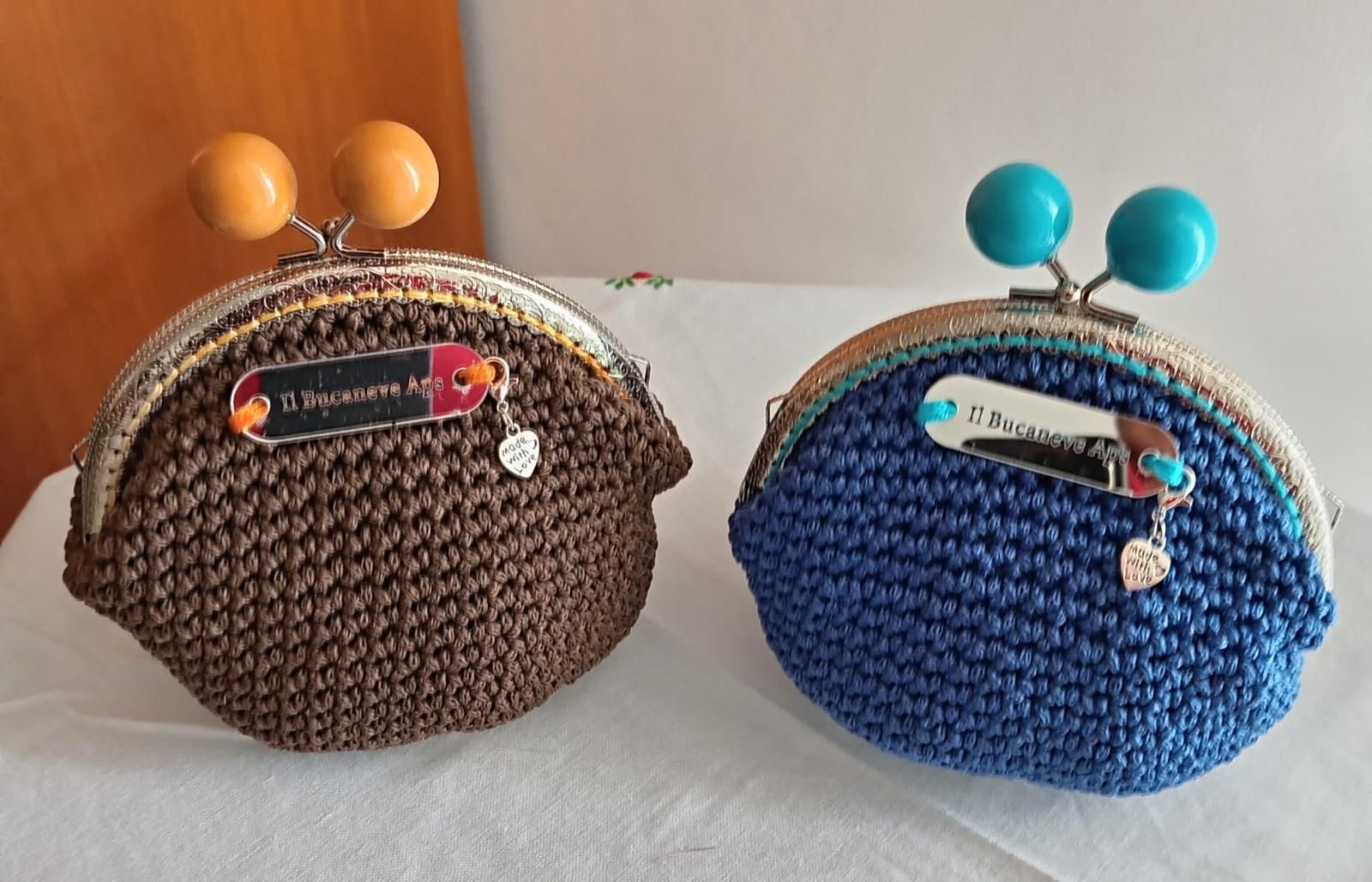 Due portamonete in maglia, uno marrone e uno blu, con chiusure a sfera su una superficie bianca.