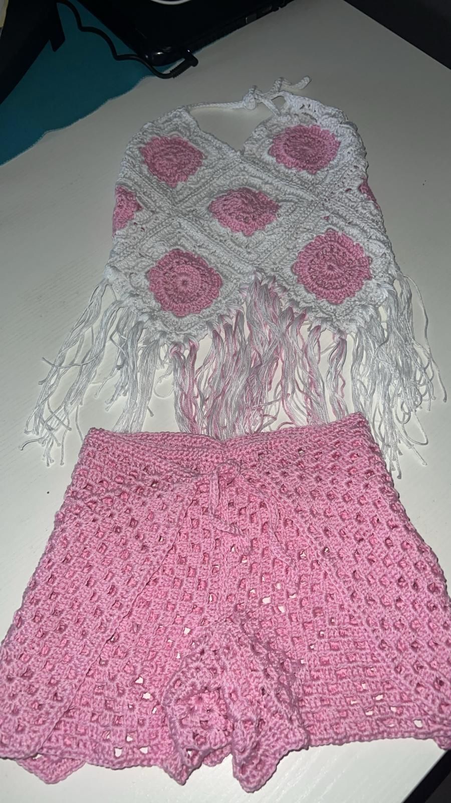 Completo rosa all'uncinetto con top bianco con frange e gonna rosa abbinata appoggiata su una superficie