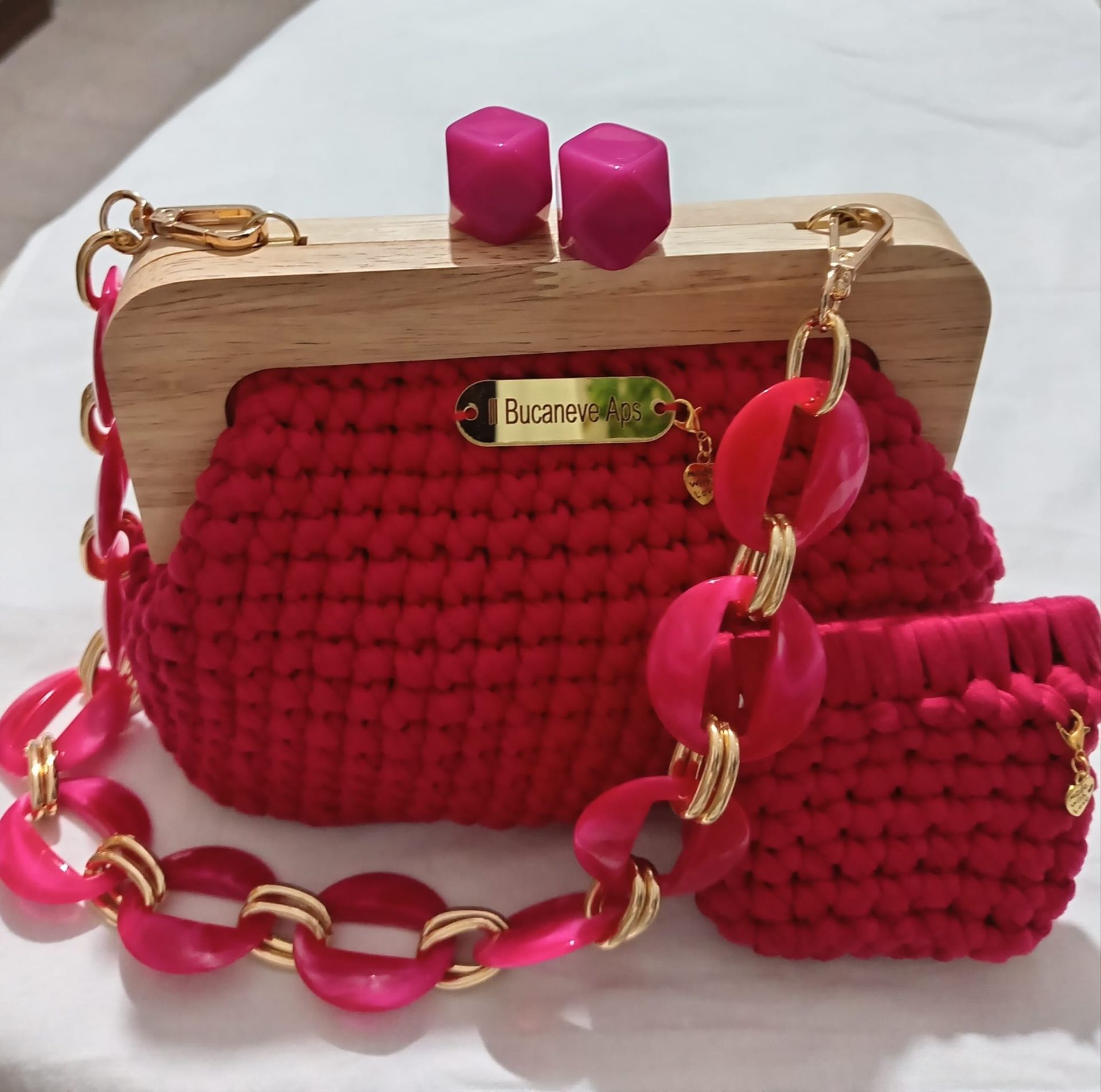 Borsa a mano rossa all'uncinetto con struttura in legno, tracolla a catena dorata e pochette coordinata su sfondo bianco.