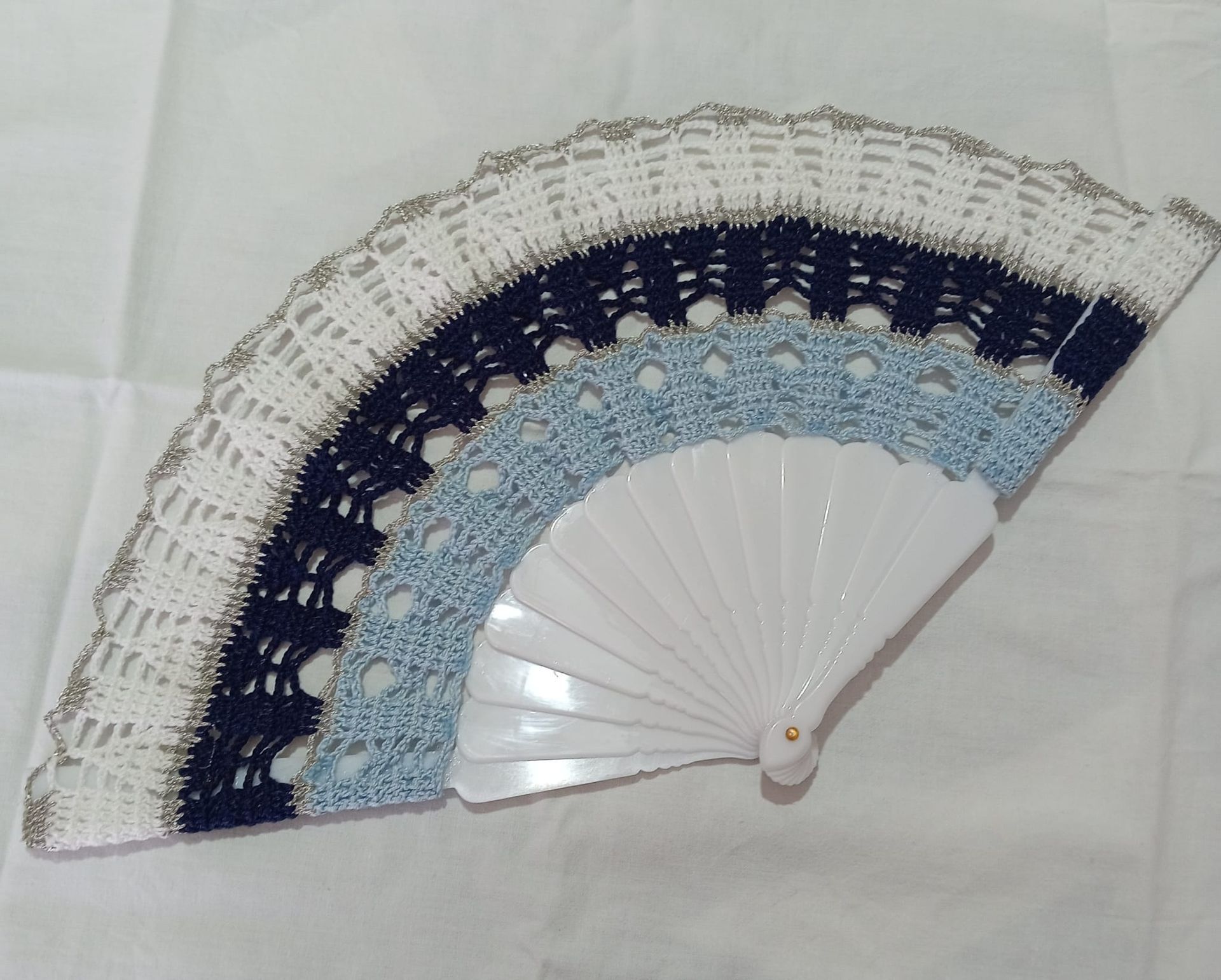 Ventaglio decorativo pieghevole con bordo in pizzo bianco, azzurro e blu navy su sfondo bianco.