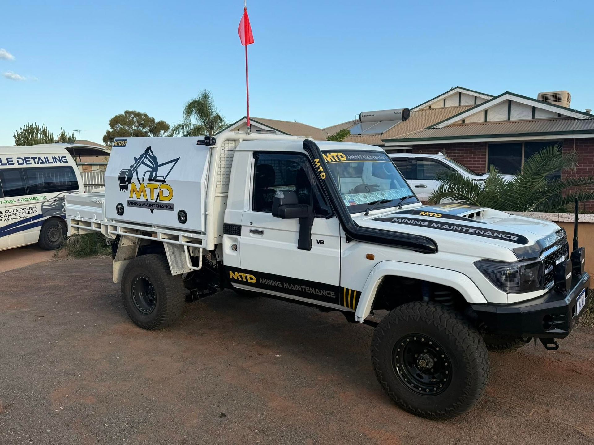 White off-road utility truck parked on a street, with a red flag and buildings in the background.