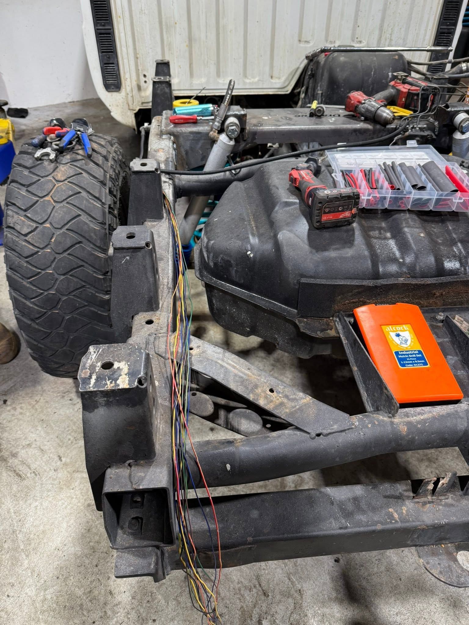 Close-up of a go-kart chassis with a black seat, orange battery pack, and rear tire in a garage
