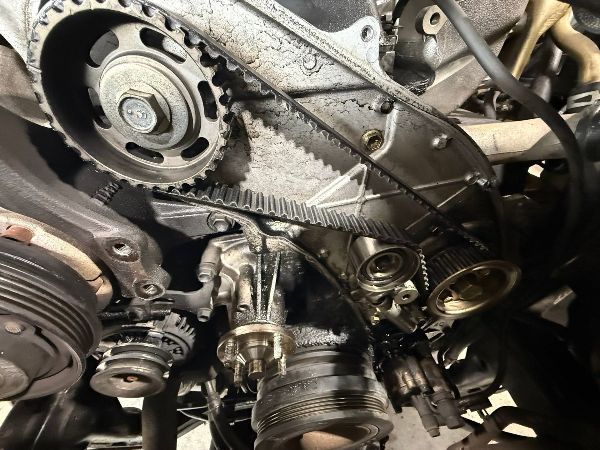 Engine timing components with belts, pulleys, and greasy metal parts exposed inside a vehicle.