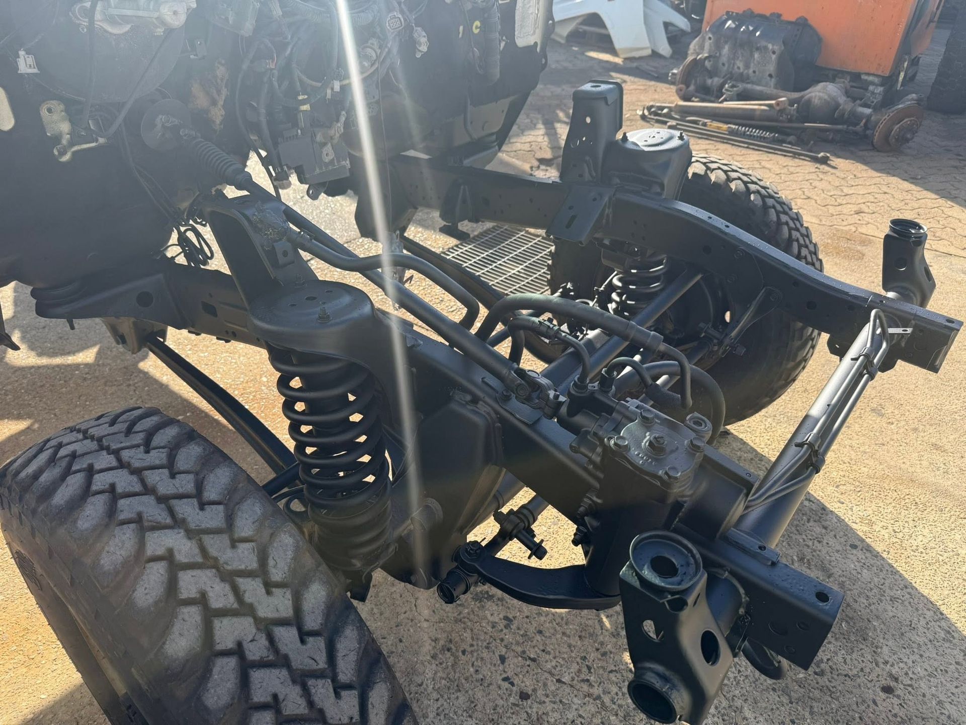 Off-road vehicle chassis with large tires and suspension in a dirt lot, missing body panels.