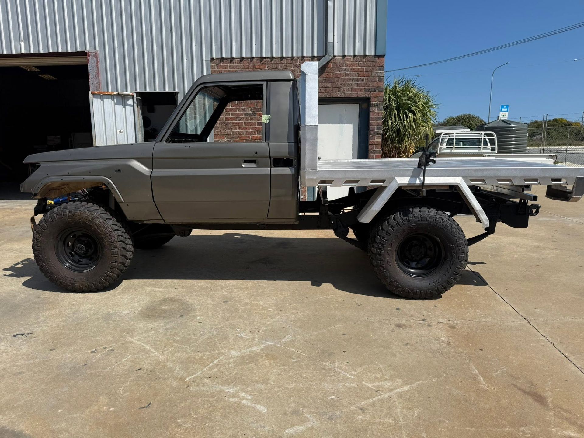 Custom gray off-road pickup truck parked beside an industrial building with a flatbed rear end